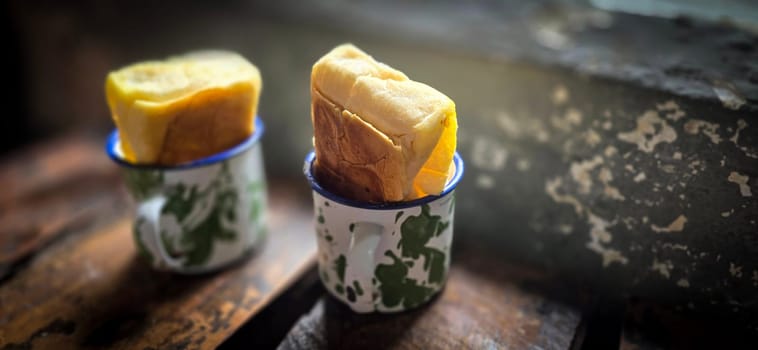 Ice chocolate drink on a vintage Indonesian iron mug with random green pattern called Blirik cup or cangkir Blirik on bokeh background along with chocolate filling bread on a cafe in Bogor