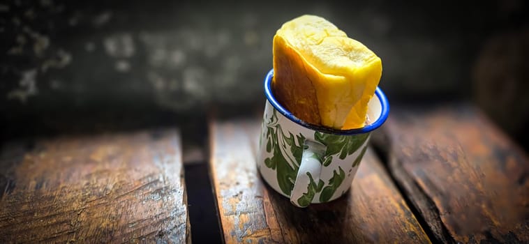 Ice chocolate drink on a vintage Indonesian iron mug with random green pattern called Blirik cup or cangkir Blirik on bokeh background along with chocolate filling bread on a cafe in Bogor