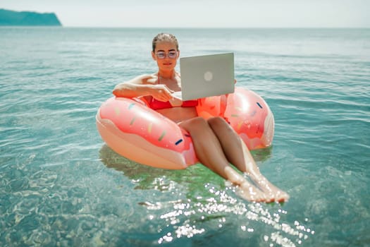 Woman laptop sea. Freelancer woman in sunglases floating on an inflatable big pink donut with a laptop in the sea. People summer vacation rest lifestyle concept