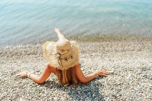 Beach Relaxation woman in hat sits on a pebble beach enjoying the sunshine. The concept of travel, vacation at sea.