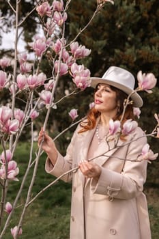 Woman magnolia flowers, surrounded by blossoming trees, hair down, white hat, wearing a light coat. Captured during spring, showcasing natural beauty and seasonal change