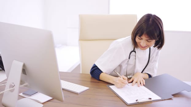 Female doctor filling a medical report sitting on the desk of a clinic