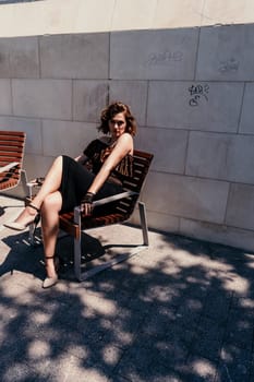 Portrait of a woman on the street. An attractive woman in a black dress is sitting on a bench outside