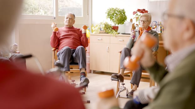 Group of senior men and women exercising in a nursing home using dumbbells and pedals