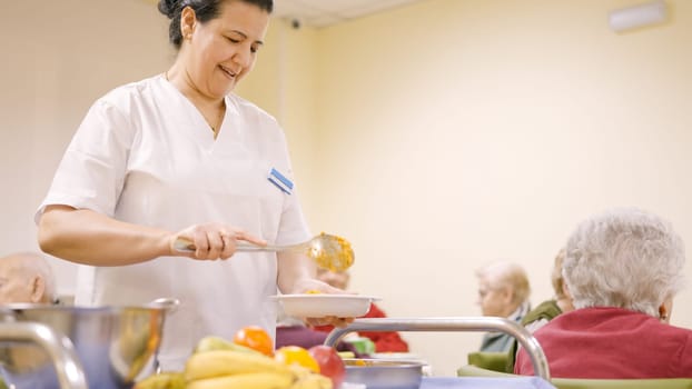 Female smiling cook serving food to old people in a geriatric