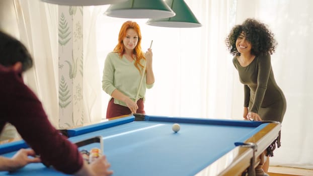 A group of diverse friends playing billiards in apartment