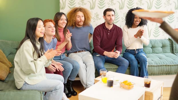 Multi-ethnic friends talking while a woman arriving with pizzas and they celebrating