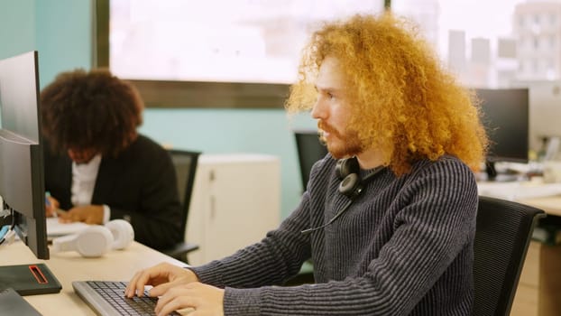Modern concentrated man with curly hair working in coworking