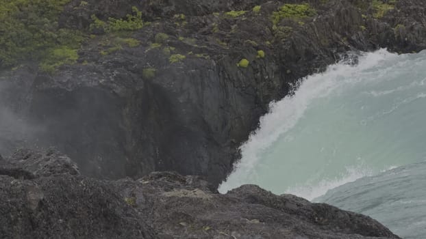 Stunning slow-mo of a turquoise glacier waterfall in a misty canyon with gentle rain.