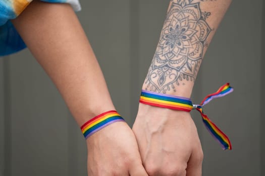 Close up of lesbian couple hands holding together showing love with rainbow bracelets.