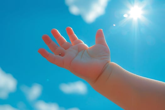 Baby hand reaching for the sun in blue sky with clouds. Concept of hope, future, childhood, and dreams