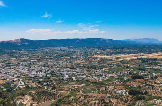 Beautiful panoramic view of a village with vegetation and roads located on a plain near mountains with a blue sky in Greece on the island of Rhodes on a summer sunny day, close-up side view.