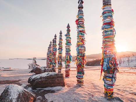 Traditional buryat shaman sacred pillars with colorful ribbons in winter at sunset, cape Burkhan, Olkhon island. Winter Baikal.