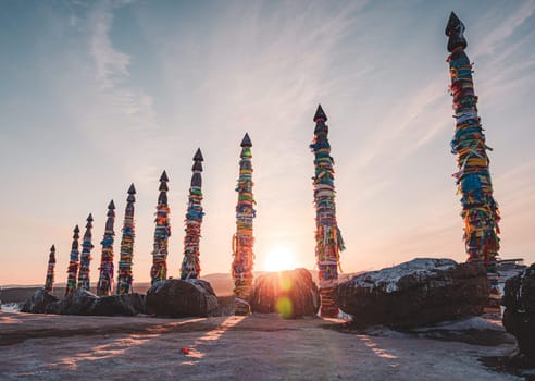 Traditional buryat shaman sacred pillars with colorful ribbons in winter at sunset, cape Burkhan, Olkhon island. Winter Baikal.