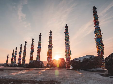 Traditional buryat shaman sacred pillars with colorful ribbons in winter at sunset, cape Burkhan, Olkhon island. Winter Baikal.