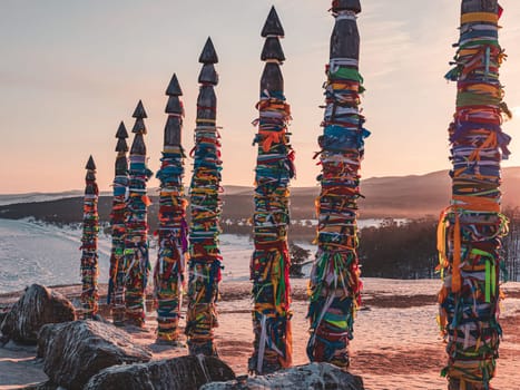 Traditional buryat shaman sacred pillars with colorful ribbons in winter at sunset, cape Burkhan, Olkhon island. Winter Baikal.