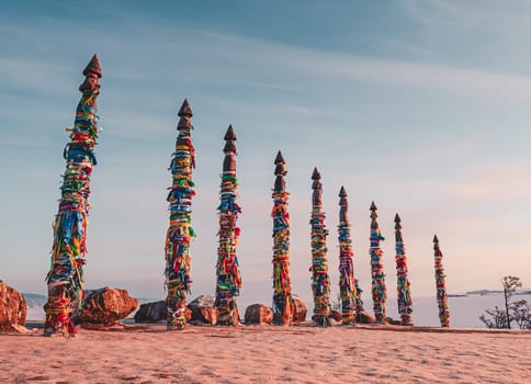 Traditional buryat shaman sacred pillars with colorful ribbons in winter at sunset, cape Burkhan, Olkhon island. Winter Baikal.