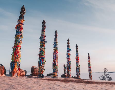 Traditional buryat shaman sacred pillars with colorful ribbons in winter at sunset, cape Burkhan, Olkhon island. Winter Baikal.