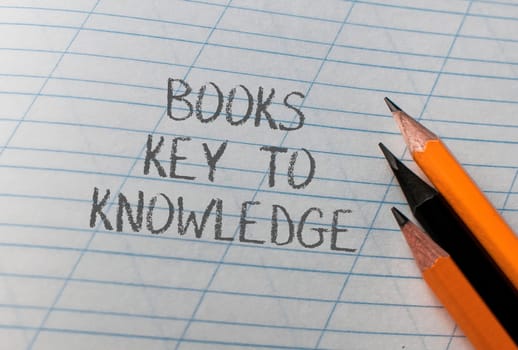 A piece of paper with the words books key to knowledge written on it. There are two pencils on the paper, one on the left and one on the right