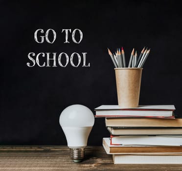 A blackboard with the words Go to School written on it. A light bulb is on top of the books and a pencil holder is on top of the books