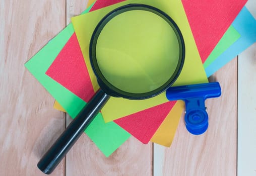 Colorful adhesive paper with magnifying glass on wooden desk. Copy space.
