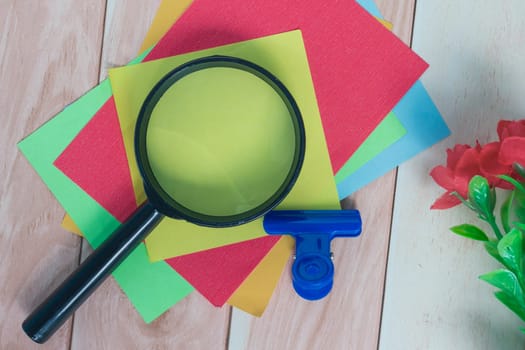 Colorful adhesive paper with magnifying glass on wooden desk. Copy space.
