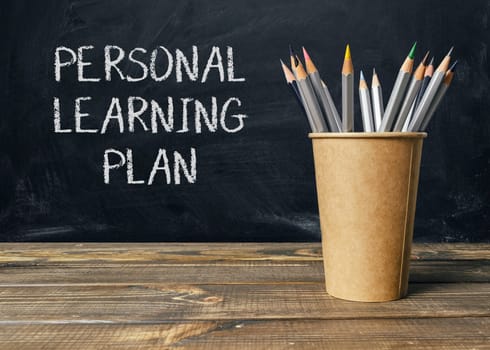 A wooden table with a cup of pencils and chalkboard with the words personal learning plan written on it