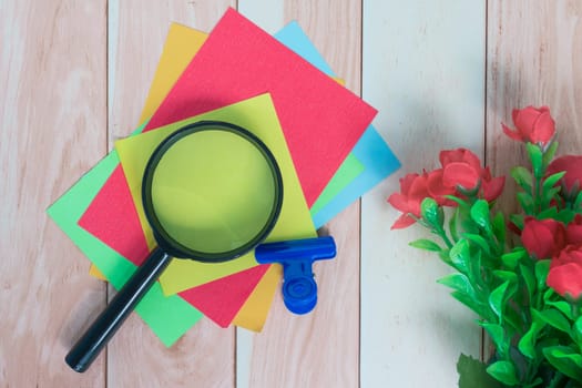 Colorful adhesive paper with magnifying glass on wooden desk. Copy space.