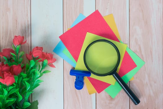 Colorful adhesive paper with magnifying glass on wooden desk. Copy space.