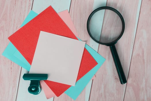 Colorful adhesive paper with magnifying glass on wooden desk. Copy space.