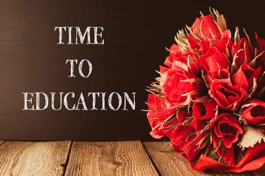 A bouquet of red flowers sits on a wooden table with the words Time to Education written below it