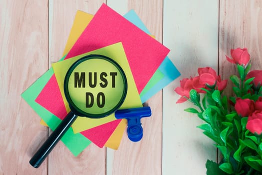 Must do word on colorful adhesive paper with magnifying glass on wooden desk.