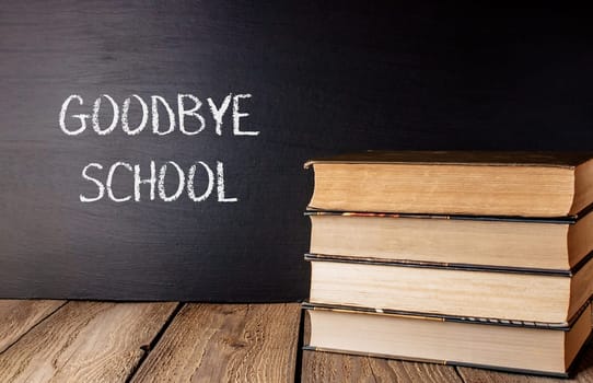 A stack of books with the word Goodbye School written on a chalkboard. The books are piled on top of each other, creating a sense of nostalgia and longing for the past