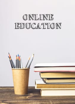 A stack of books and a pencil holder on a table with the words online education written above them