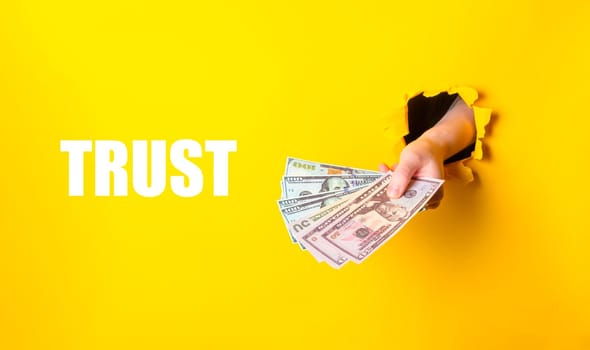 A hand holding a stack of money with the word trust written below it. Concept of financial security and the importance of trust in financial transactions