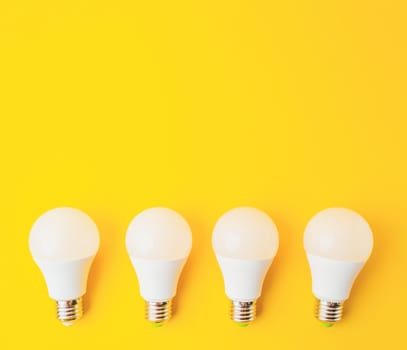 Four white light bulbs are arranged on a yellow background. The bulbs are all the same size and shape, and they are evenly spaced out. Concept of uniformity and order, as the bulbs are all identical