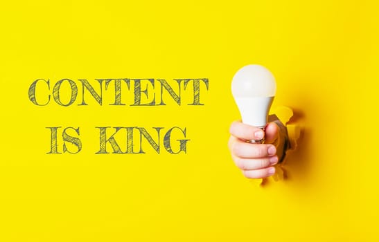 A person holding a light bulb with the words content is king written behind them. The image conveys the idea that content is king, emphasizing the importance of creating valuable and engaging content