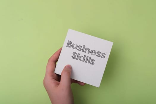 A hand holding a piece of paper with the word business skills written on it. Concept of someone learning or practicing business skills, possibly in a classroom or workshop setting