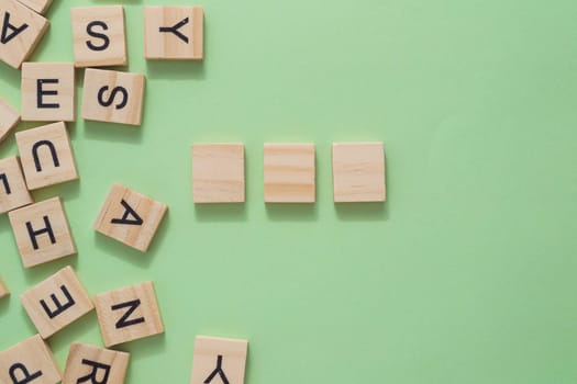 Three wooden blocks are on a green background with the letters scattered around them. copy space