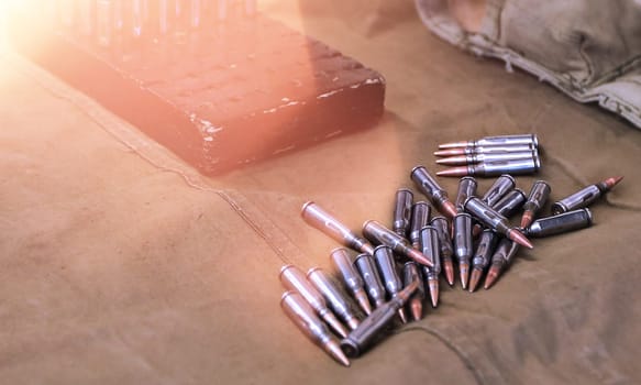 A soldiers hand is carefully reaching into a wooden box to hold a single bullet, while scattered bullets are arranged on an olive drab cloth surface, creating a compelling sense of depth and focus.