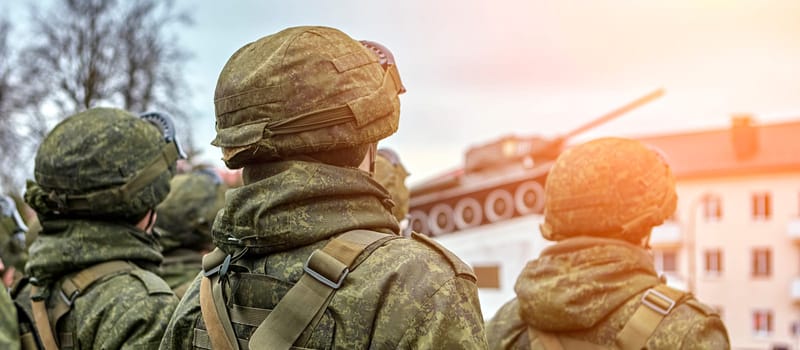 Several soldiers wearing camouflage uniforms stand in a row, holding guns and looking prepared for a mission. The background is blurred, highlighting their readiness and determination.