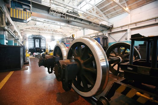 The workshop showcases the maintenance of railway equipment with a focus on a locomotive and a set of gleaming train wheels. Workers are possibly present, tending to the overhaul and repair of these vital components that keep the transportation network running smoothly. The setting suggests routine upkeep, keeping safety and efficiency at the forefront.