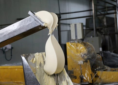 A large portion of uncooked dough flows from a metal chute into a processing container at an industrial bakery. The equipment is designed for high-volume production, facilitating the efficient preparation of dough for subsequent baking stages.