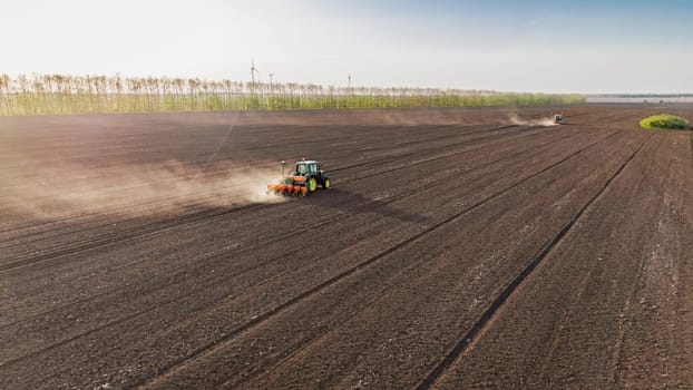 Aerial view of a tractor tilling the soil in a vast land lot, with a background of green grass, under a clear sky. Seeds to sow