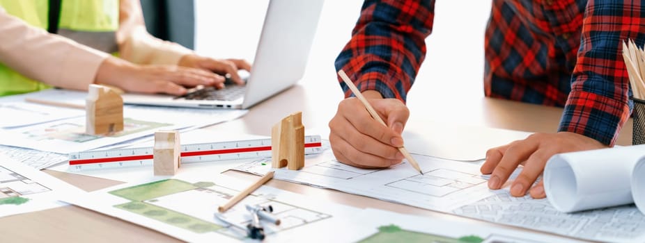 A cropped portrait of professional architect working with blueprint during safety engineer using laptop analysis data at meeting table with document scatter around. Close up. Delineation.