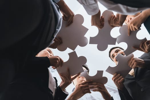 Below view of diverse corporate officer workers collaborate in office connecting puzzle pieces as partnership and teamwork concept. Unity and synergy in business idea by merging jigsaw puzzle. Concord