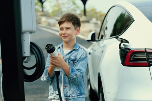 Little boy recharging eco-friendly electric car from EV charging station. EV car road trip travel concept for alternative transportation powered by clean renewable and sustainable energy. Perpetual