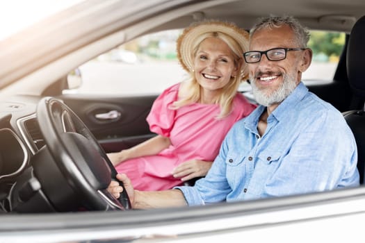 Happy retired couple enjoying a car ride, the woman wearing a hat, window down, representing freedom and joy