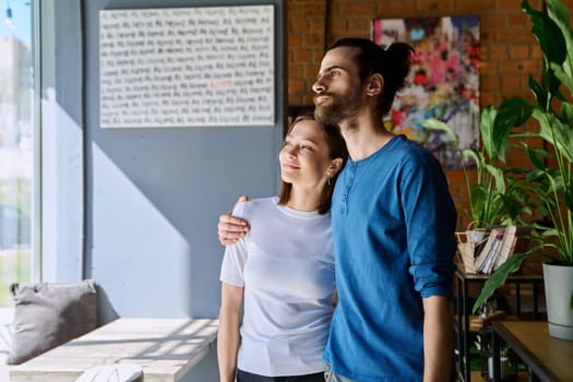 Young happy couple hugging together looking out the window. Love, friendship, romance, relationship, happiness, lifestyle, people concept