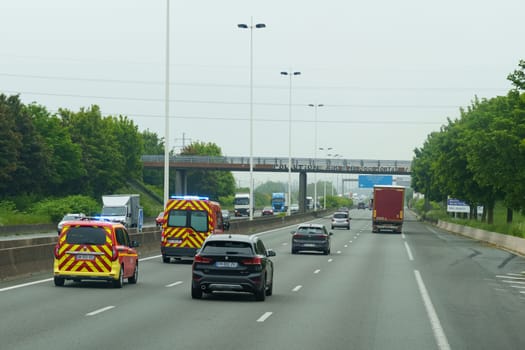 Lille, Belgium - May 22, 2023: Vehicles including emergency trucks occupy a highway under overcast skies, suggesting a scene of routine traffic alongside potential roadside assistance.